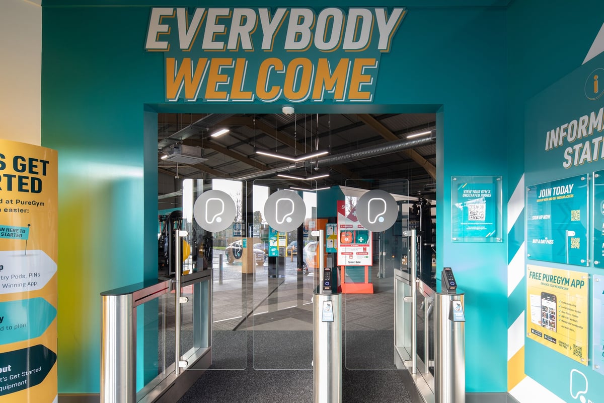 PureGym Neath: Entrance lobby with "Everybody Welcome" signage, turnstiles, and informational displays.