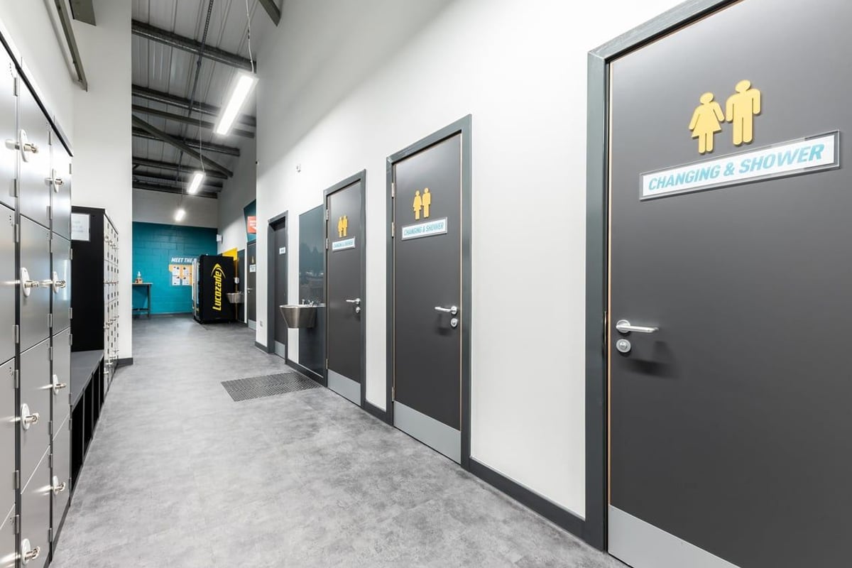 PureGym Alloa: Grey corridor with multiple changing room and shower room doors, signage indicating facilities.