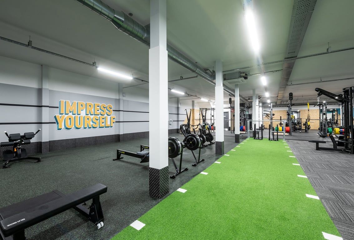 PureGym Derby Kingsway Retail Park: Weight benches, squat racks, free weights, turf area, and motivational wall text.