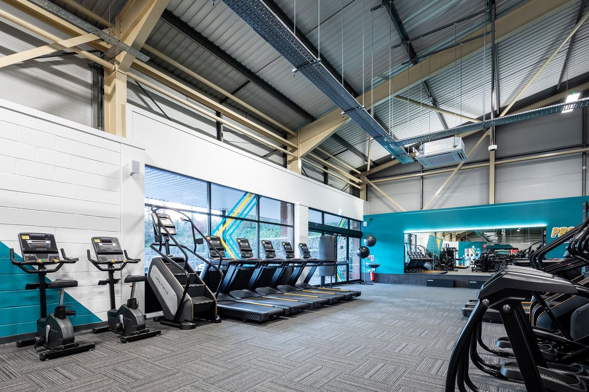 PureGym Neath: Rows of treadmills, ellipticals, and exercise bikes in a gym studio with large windows.
