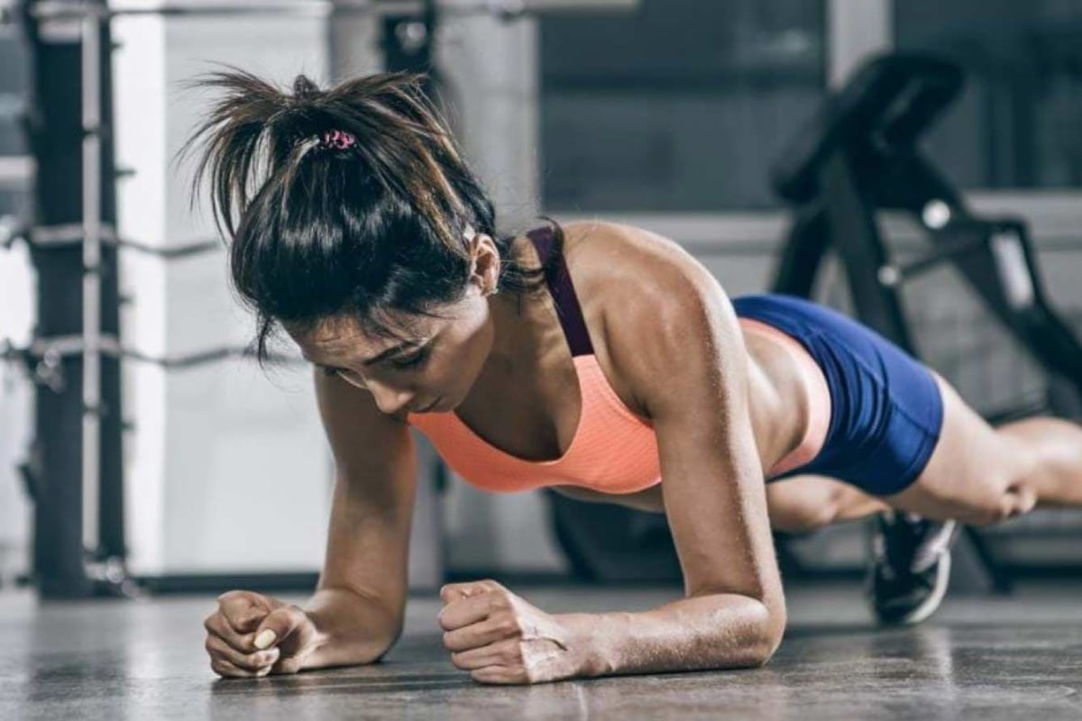 Frau in Plank-Position mit korallenfarbener Sportunterstützung und blauen Shorts im Fitnes