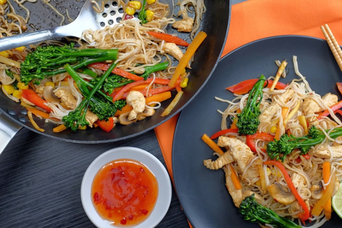 Wok and plate of noodles with turkey pieces, peppers, beansprouts and green vegetables