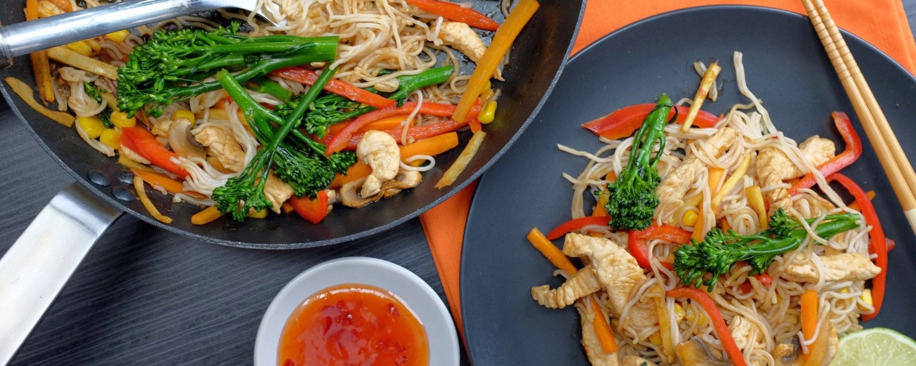 Wok and plate of noodles with turkey pieces, peppers, beansprouts and green vegetables