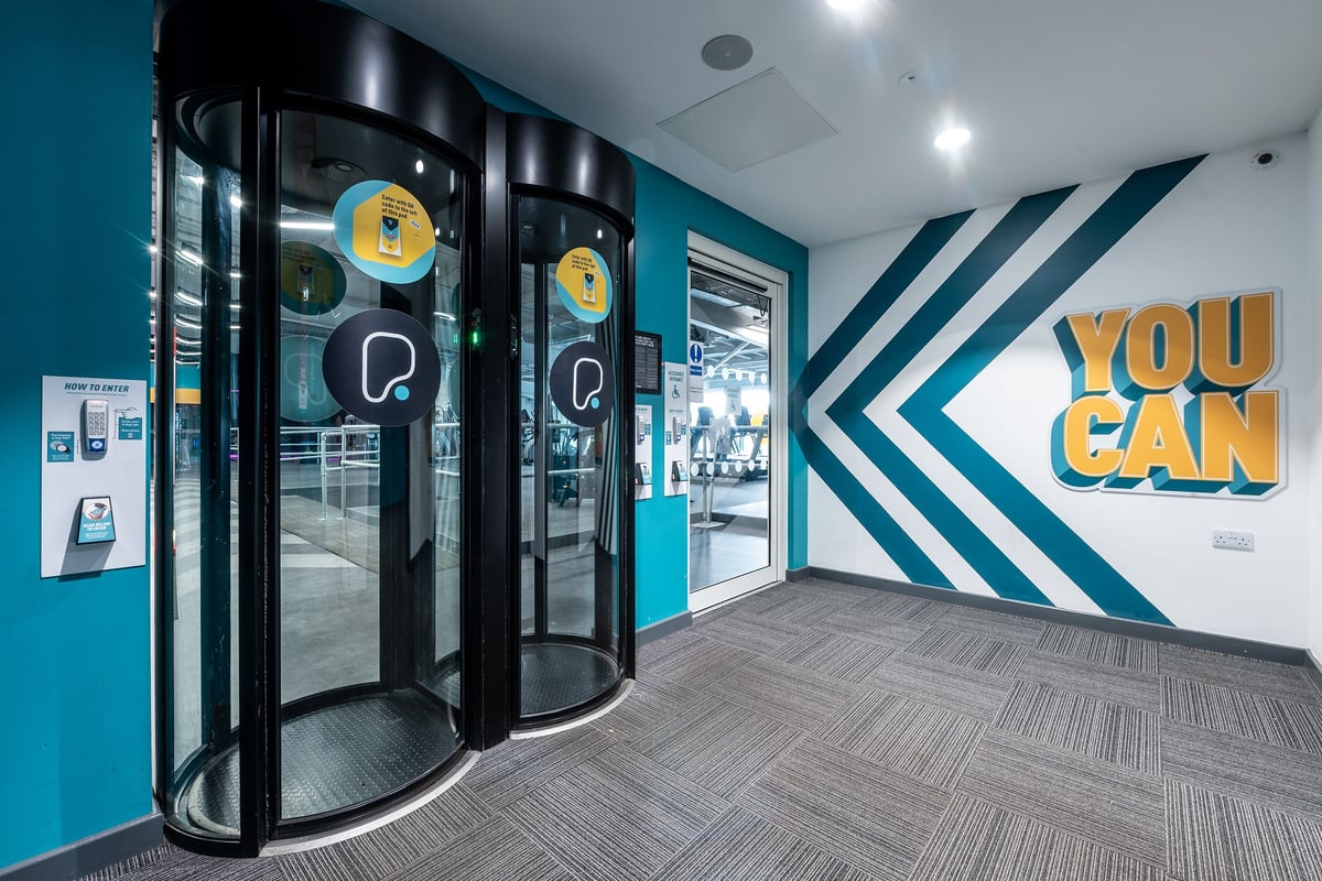 PureGym Manchester Cheetham Hill Retail Park: Glass entry doors, geometric wall graphics, and a "You Can" motivational sign.