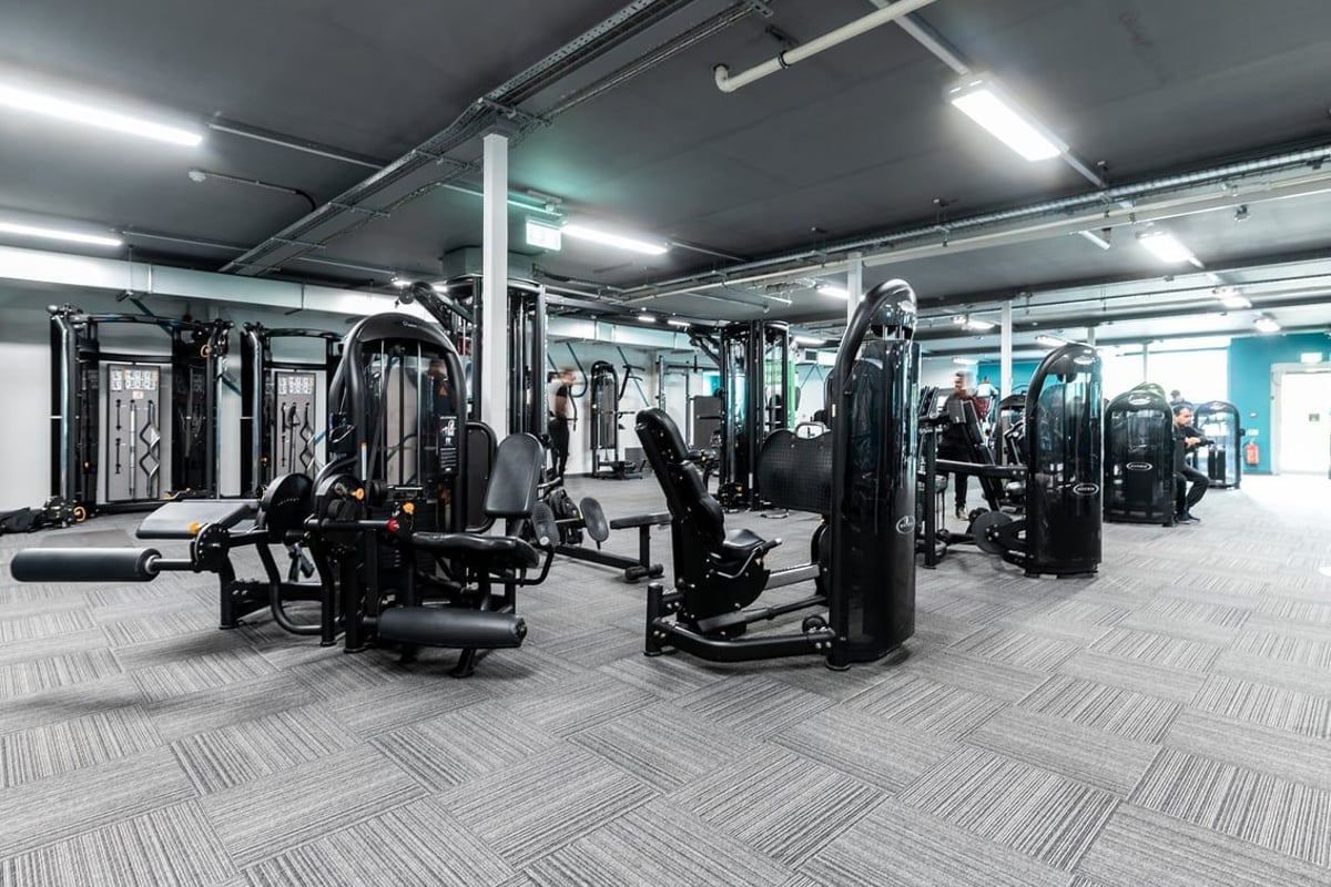 PureGym Oldham: Weight machines, resistance equipment, rubberized floor tiles in a dimly lit gym interior.