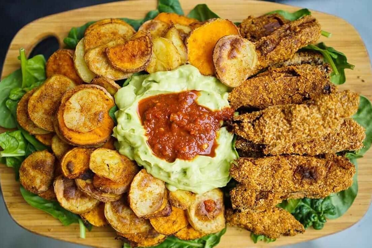 Knusprige Streifen, gewürzte Kartoffelscheiben, Guacamole und Salsa auf Spinatblättern.