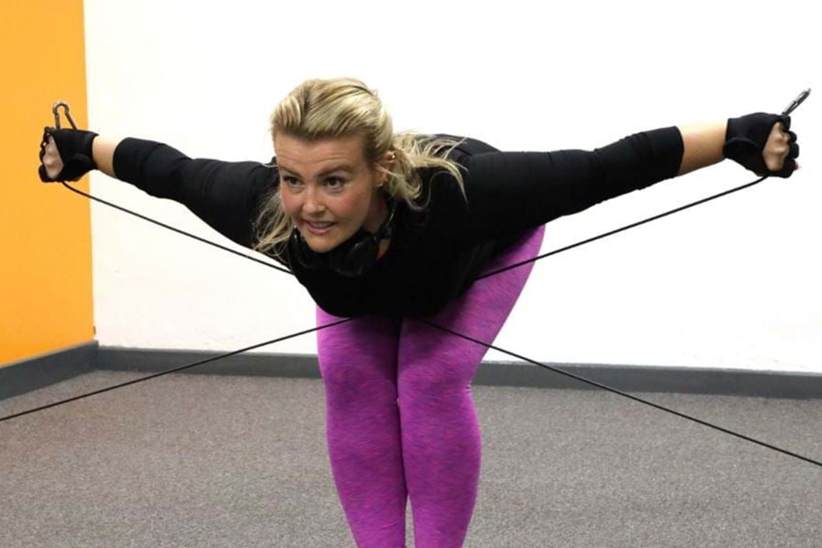Woman in purple leggings exercising with resistance bands in a room with orange wall