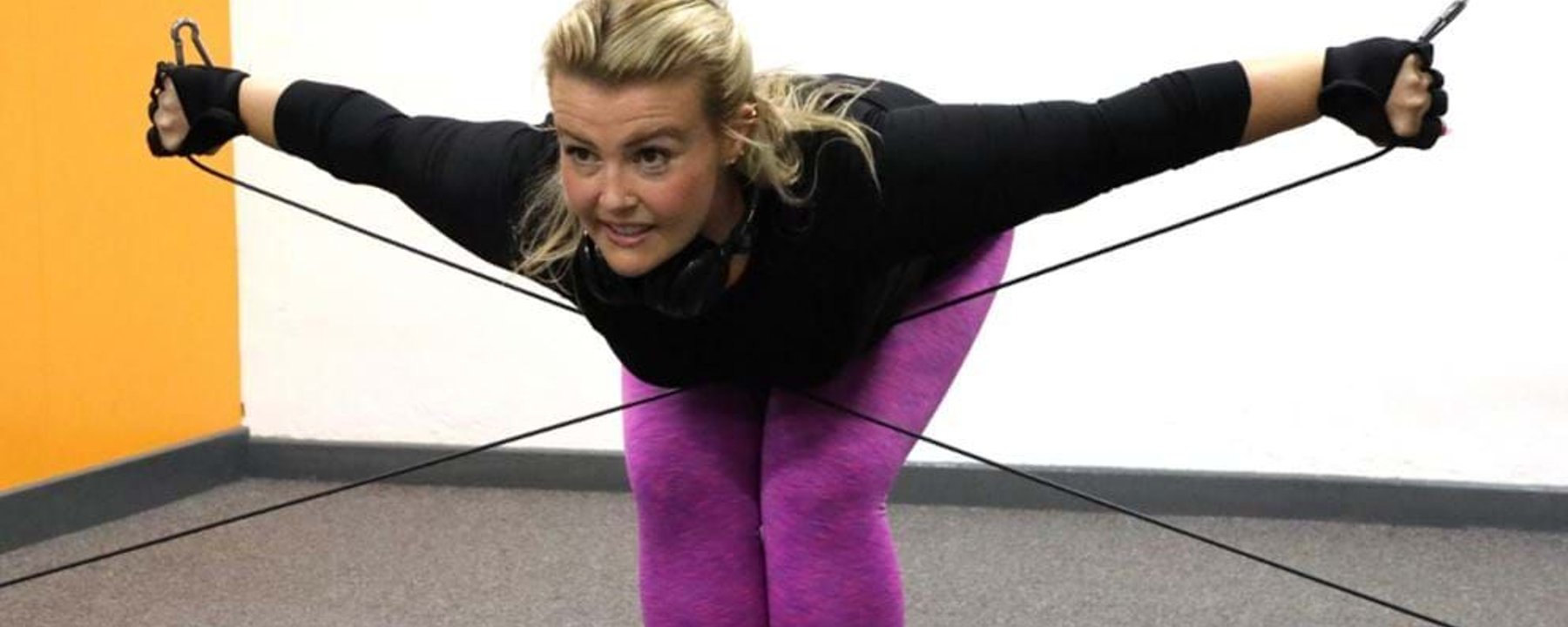 Woman in purple leggings exercising with resistance bands in a room with orange wall