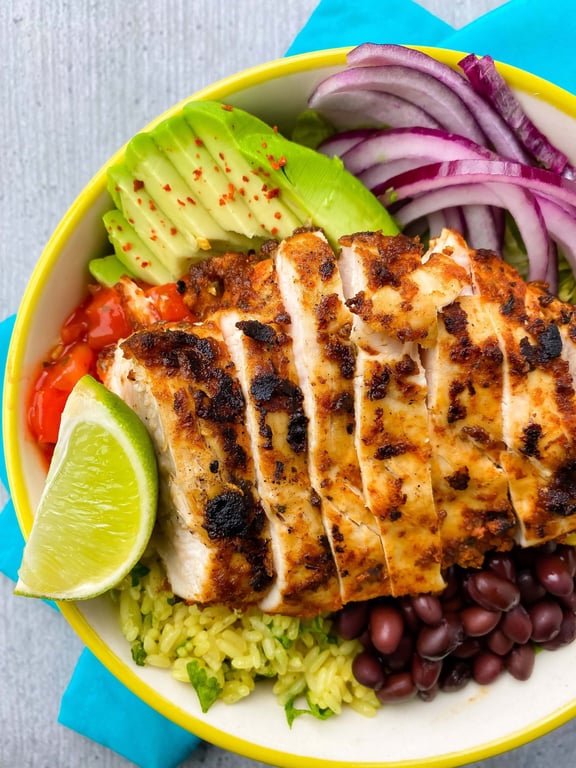 Grilled chicken slices with avocado, red onion, black beans, rice, lime wedge, and salsa