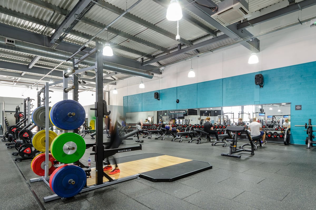 PureGym Worcester: Weight plates, squat racks, benches, rubberized flooring in industrial-style weightlifting area.