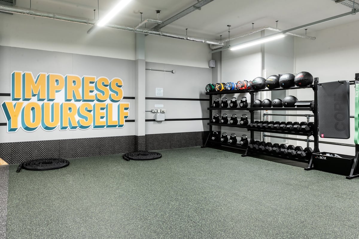 PureGym Milton Keynes Kingston Centre: Weights racks, medicine balls, mats, and wall signage saying "Impress Yourself".