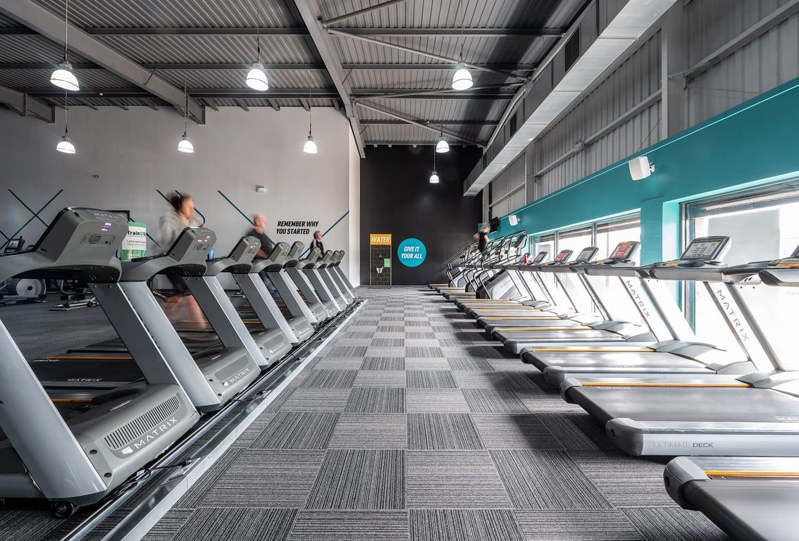 PureGym Warrington Central: Rows of treadmills in a dimly lit gym interior with pendant lighting.