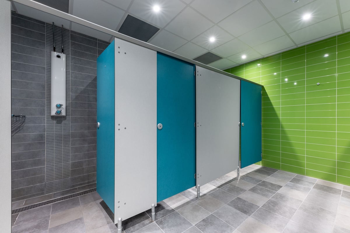 PureGym Sheffield Crystal Peaks: Rows of shower stalls in teal and green with tiled floor.
