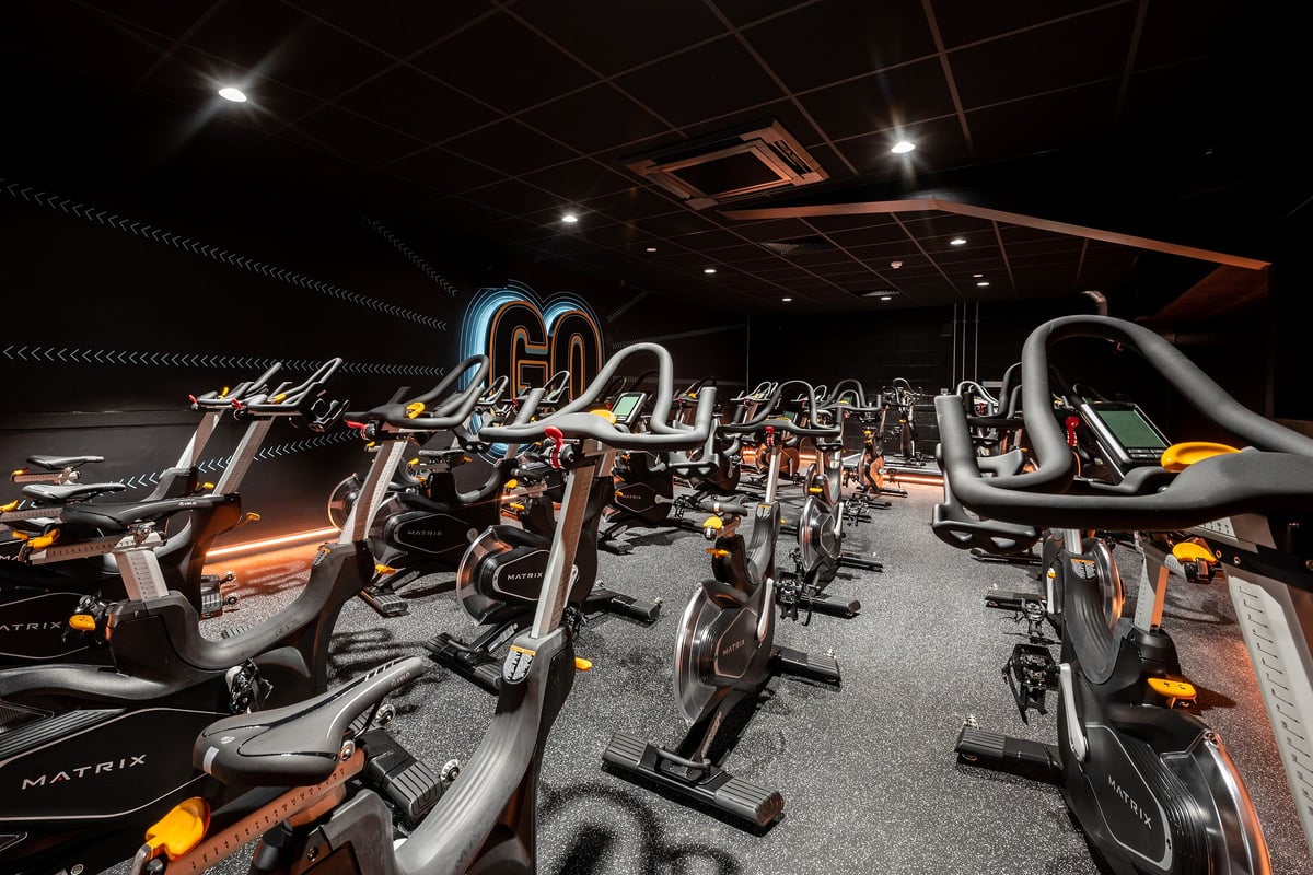 PureGym Ashford Warren Retail Park: Rows of stationary cycles with neon lighting in a dimly lit studio.