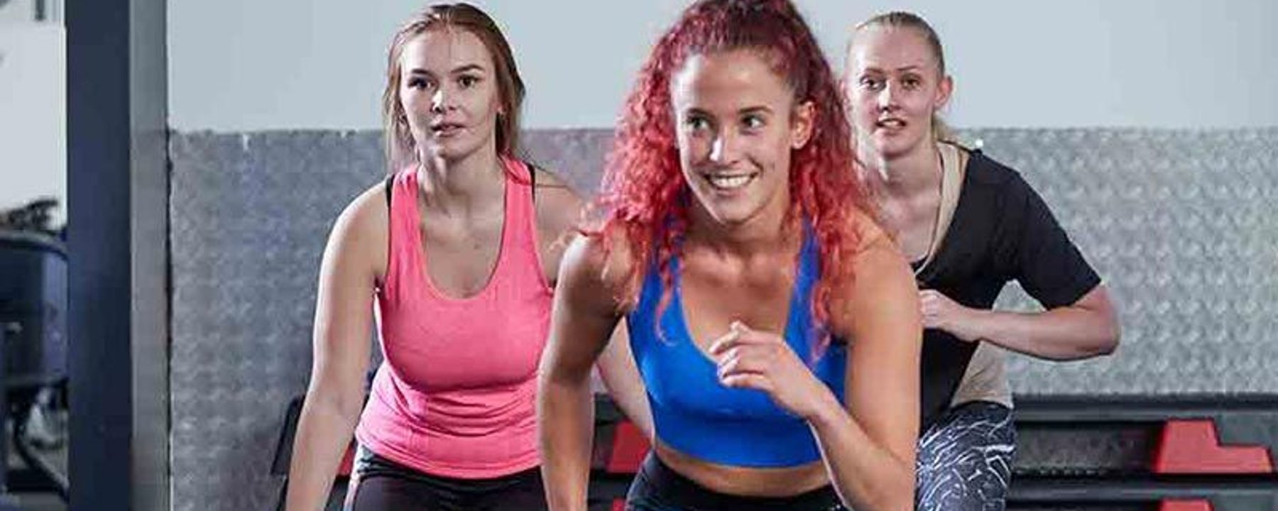 Drei Frauen trainieren drinnen in Sportkleidung und lächeln.