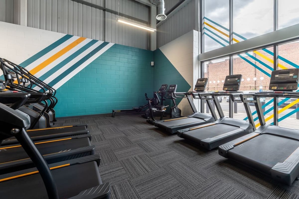 PureGym Spalding: Rows of treadmills, colourful striped wall panelling, and industrial-style lighting fixtures.