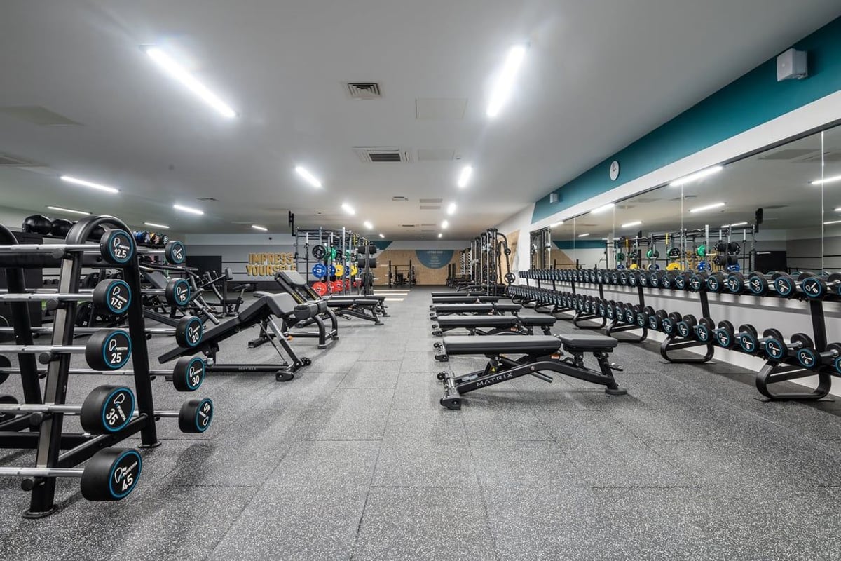 PureGym Airdrie: Rows of weight benches, dumbbells, and weight racks on rubberized flooring.