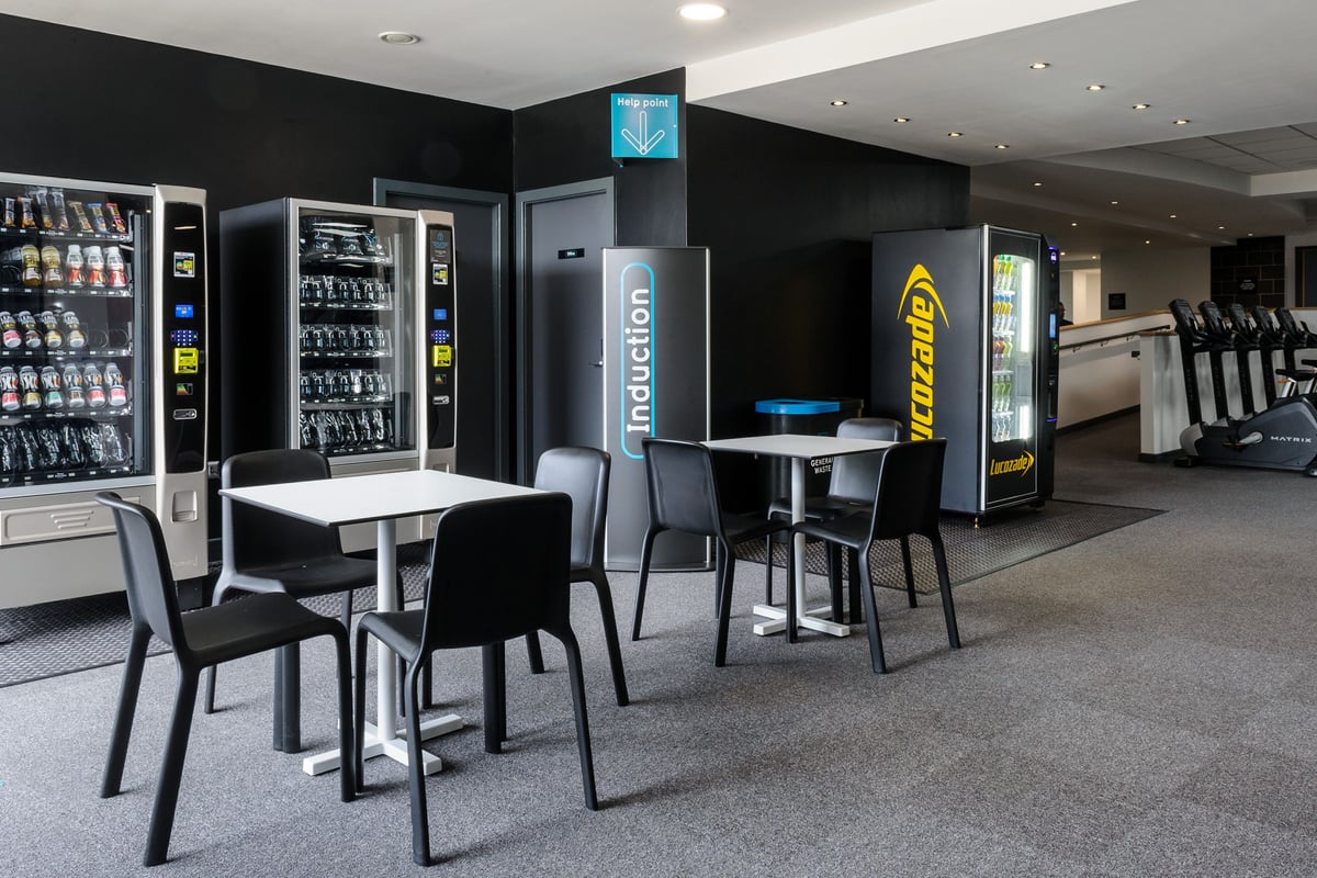 PureGym Billericay: Vending machines, tables, chairs in a minimalist black and grey setting.