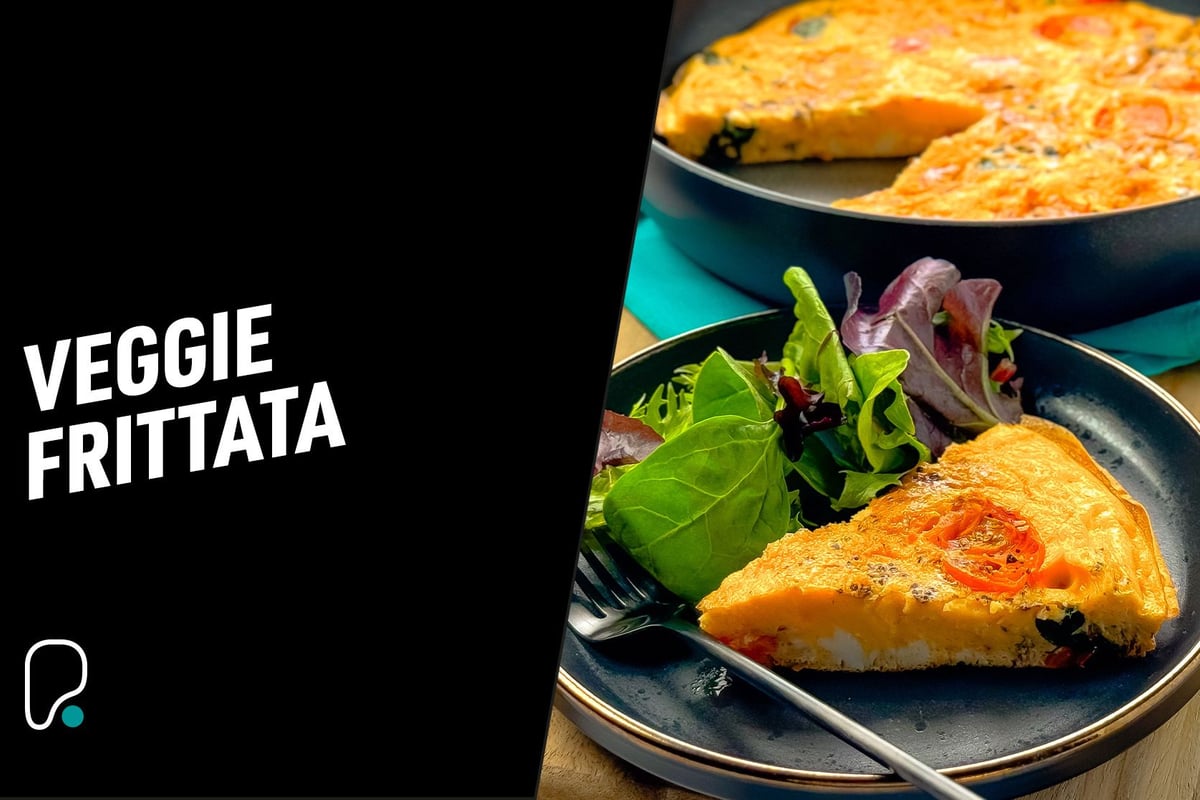 Slice of veggie frittata on a plate with mixed salad leaves and a fork nearby