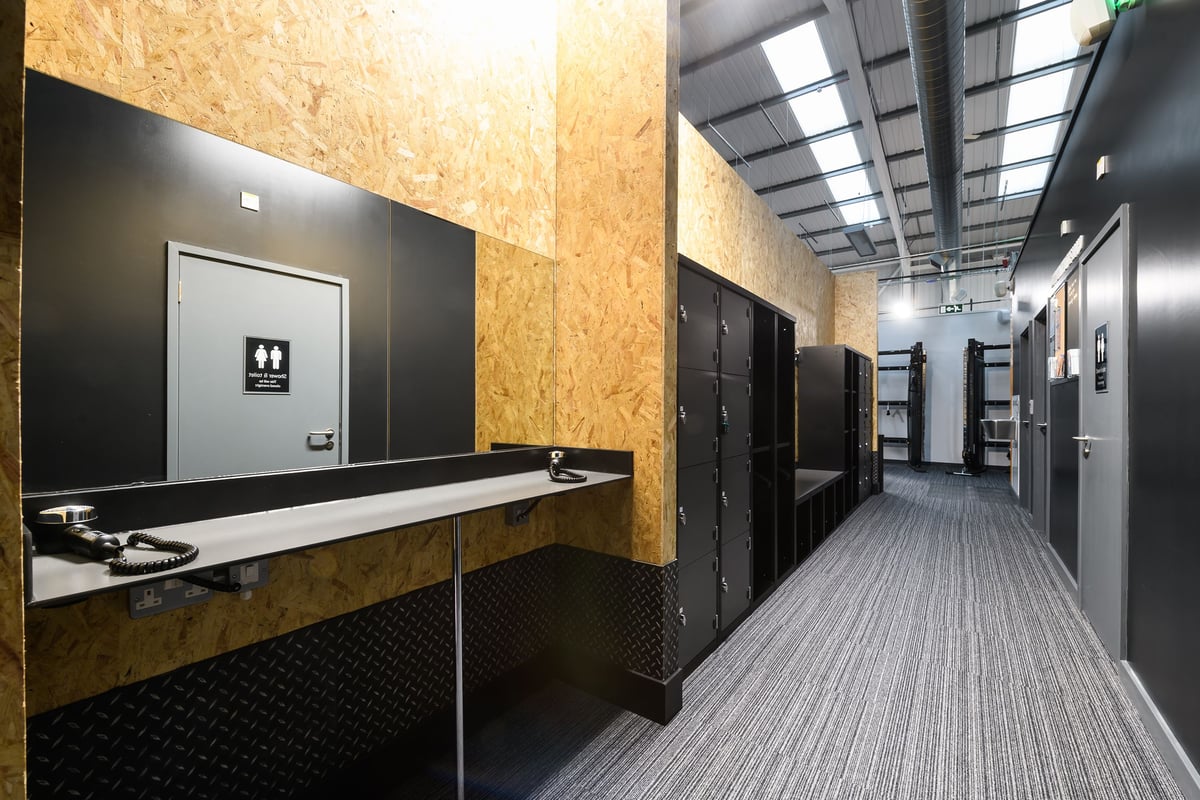 PureGym Buckingham: Bank vaults, lockers, and a long mirrored counter in a facility with OSB walls.