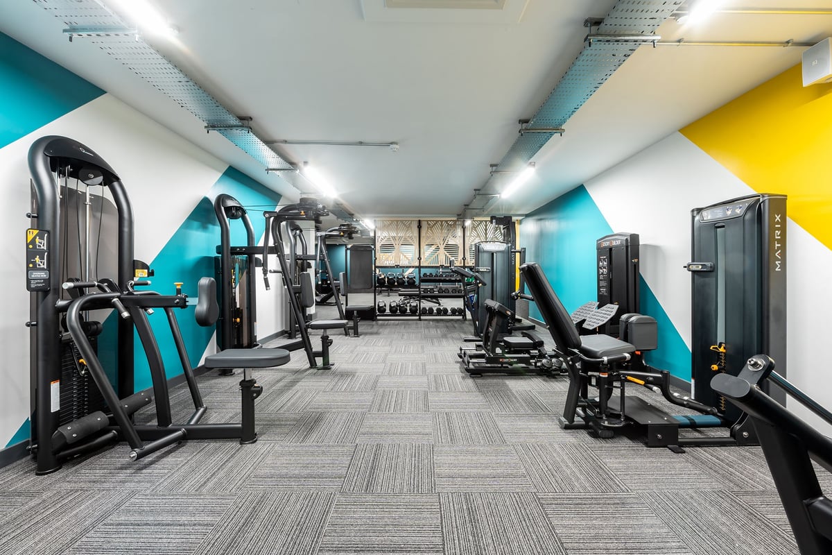 PureGym London Welling: Rows of weight machines, strength equipment, and pec decks in a teal and yellow color-schemed gym.