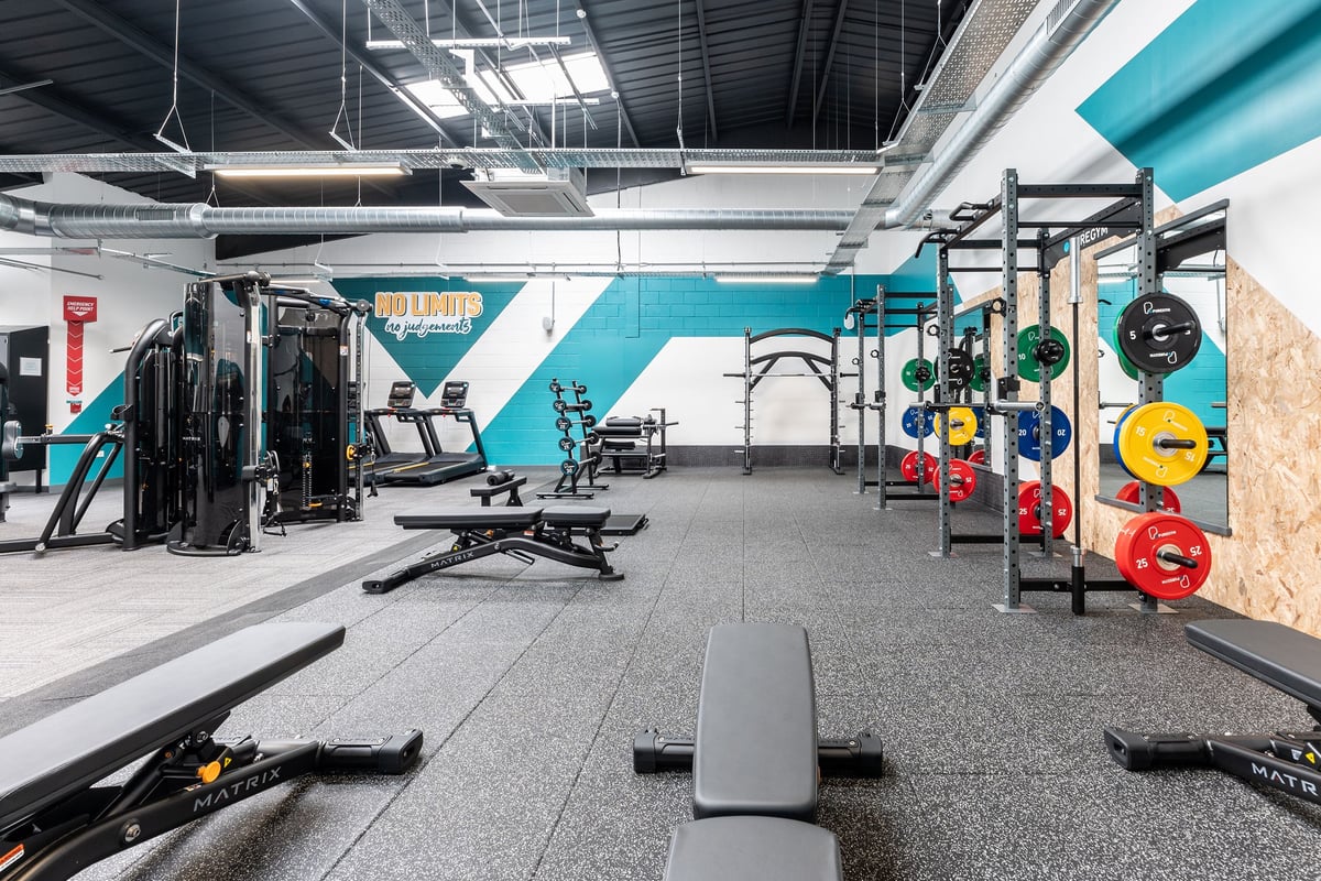 PureGym Dewsbury: Gym with weight machines, free weights, squat racks, rubberized flooring, and color accented walls.