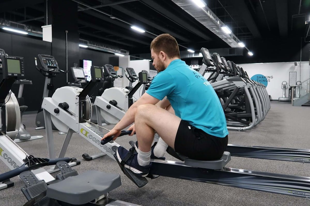 Man in blue shirt using rowing machine in gym with treadmills in background