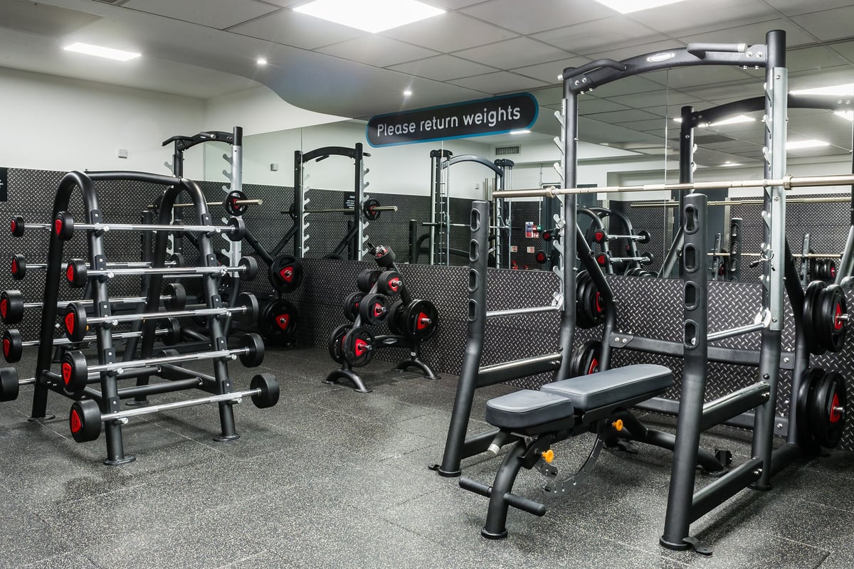 PureGym London Holborn: Gym with squat racks, weight benches, rubberized floors, mirrors, and weight racks with red plates.