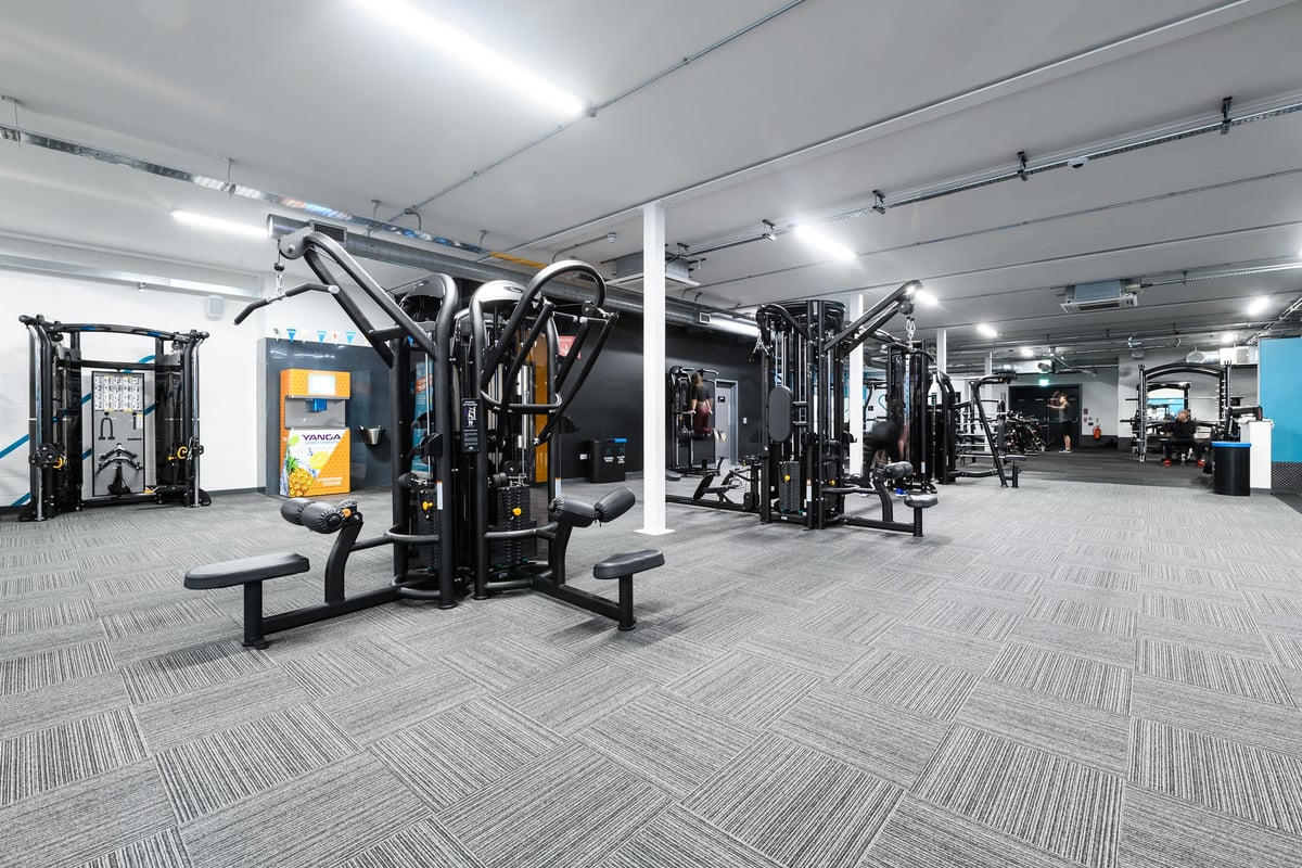 PureGym Cardiff Bay: Resistance machines, benches, free weights, mirrors, and rubberised flooring in a gym setting.