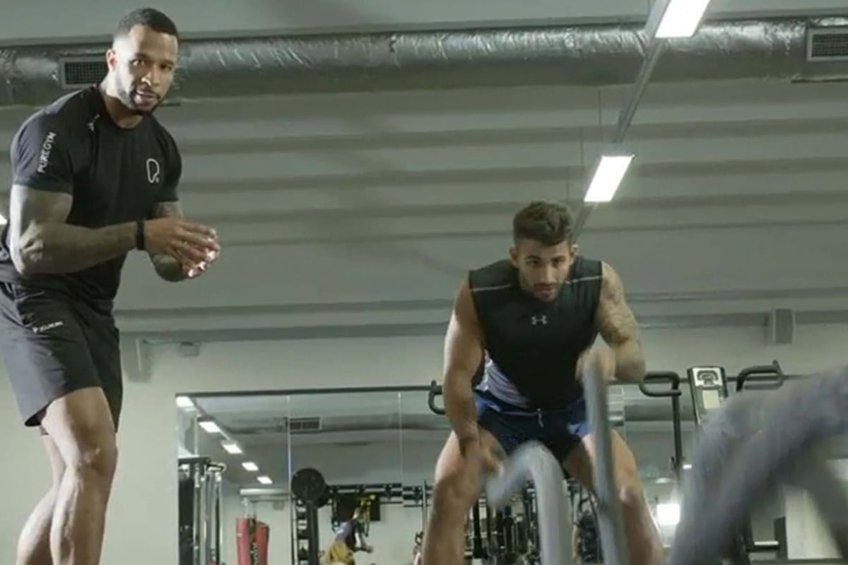 Two men exercising with battle ropes in a gym with mirrors and equipment behind them