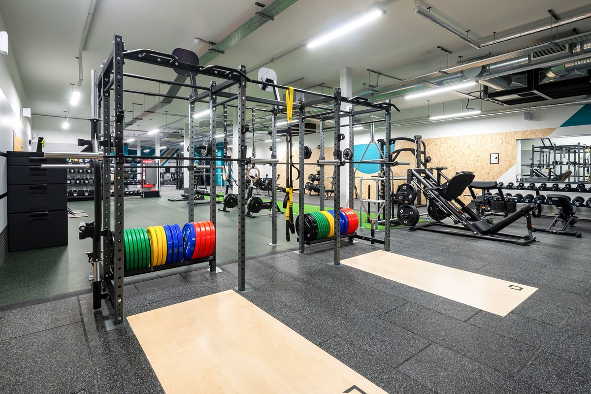 PureGym Stratford-upon-avon: Rig frames, weight plates, benches, rubberized flooring in a weight training area.