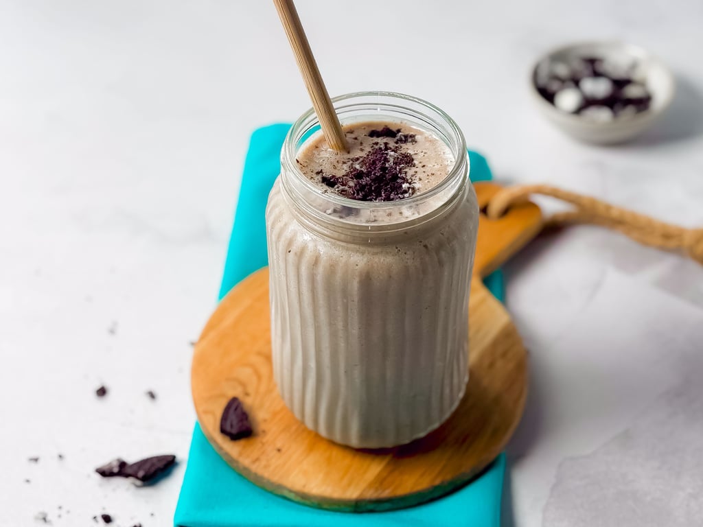 Chocolate milkshake in a glass jar with a straw on a wooden board and blue cloth