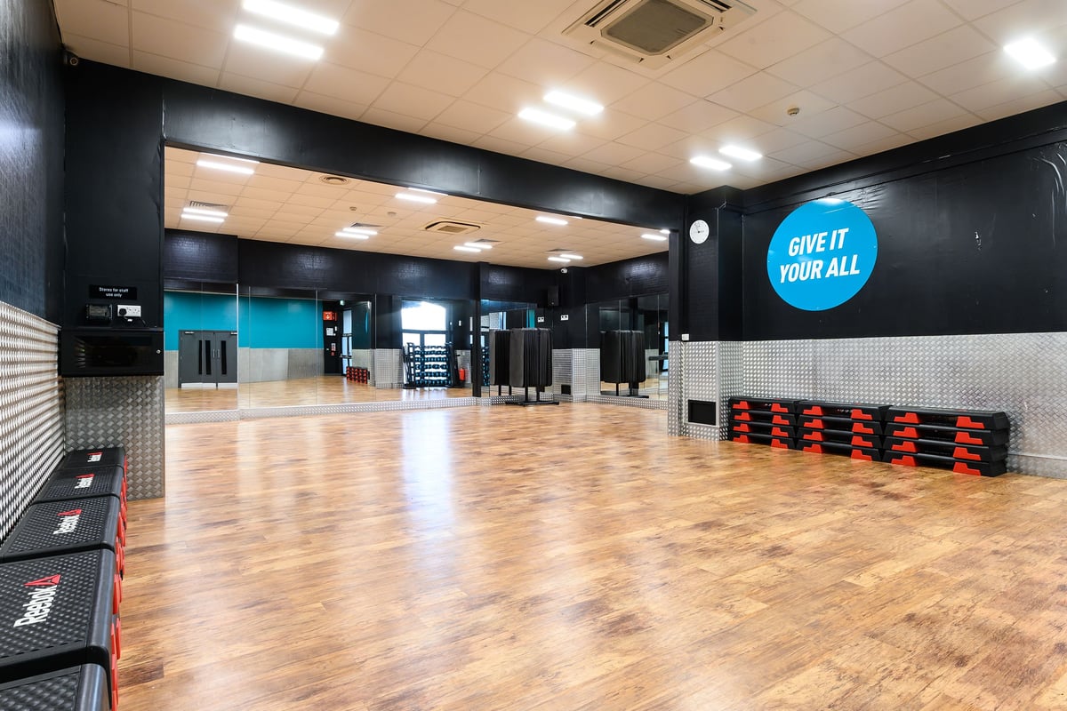 PureGym Bromborough: Large open studio space with rubberized floors, weightlifting platforms, free weights.