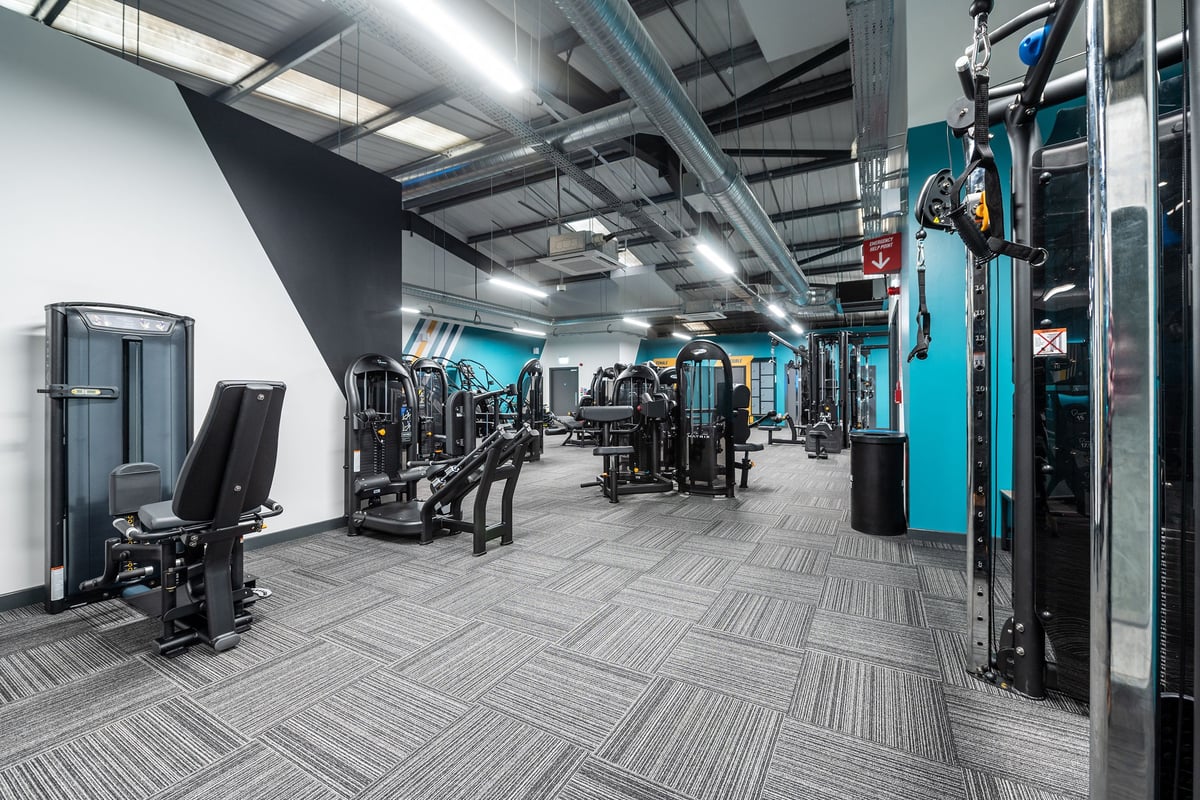 PureGym Letchworth: Weight machines, resistance equipment, patterned flooring in a dimly lit gym interior.