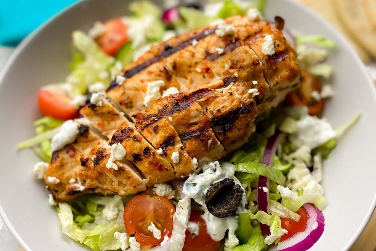 Grilled chicken breast on a salad with lettuce, cherry tomatoes, olives, and feta cheese