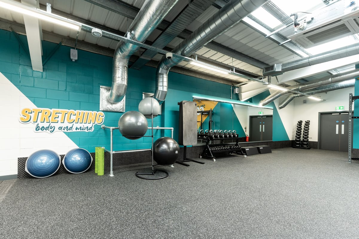 PureGym Chippenham: Stretching area with stability balls, resistance bands, exercise mats, and exposed ductwork.