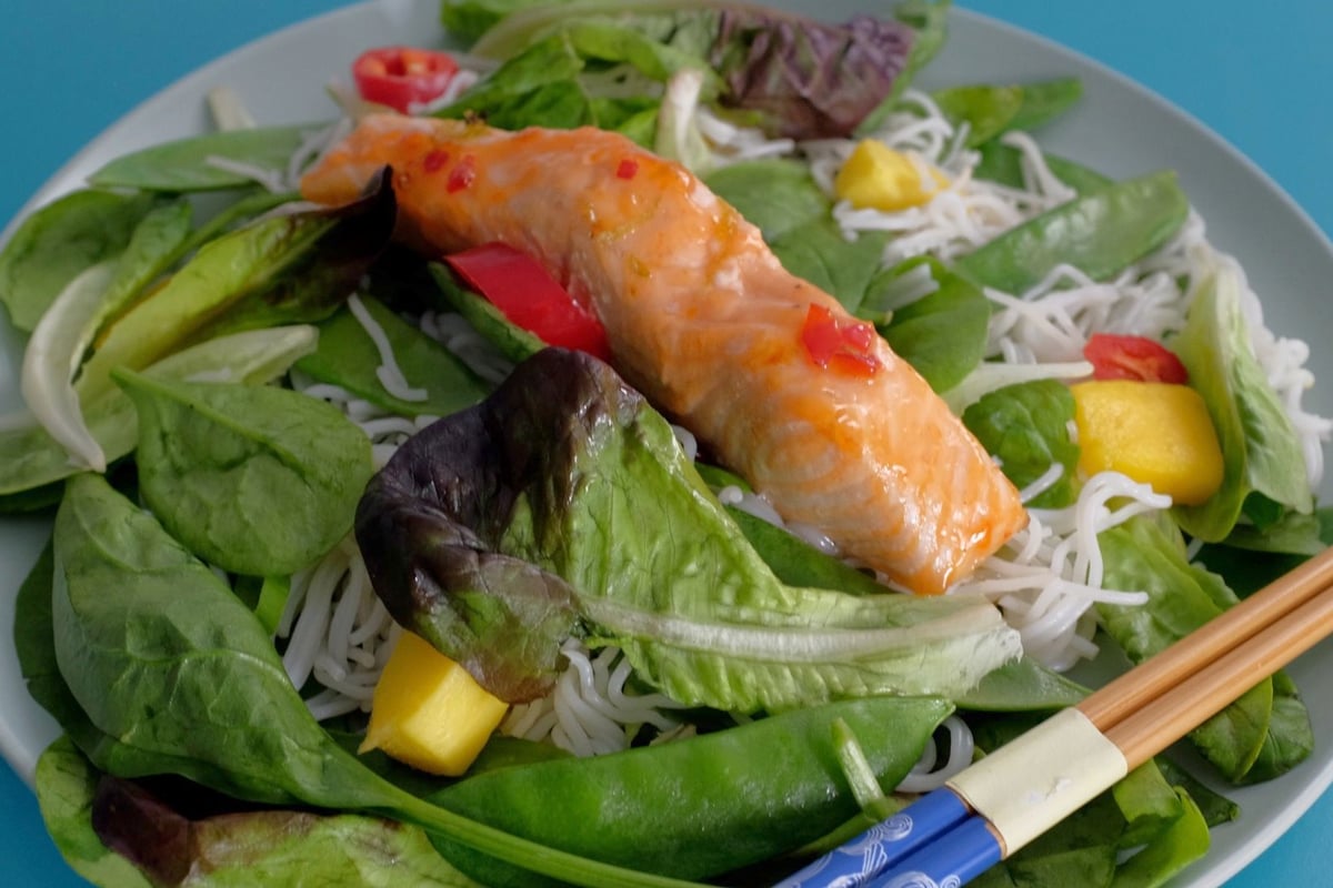 Grilled salmon fillet with rice noodles, mixed salad leaves and mango on a white plate