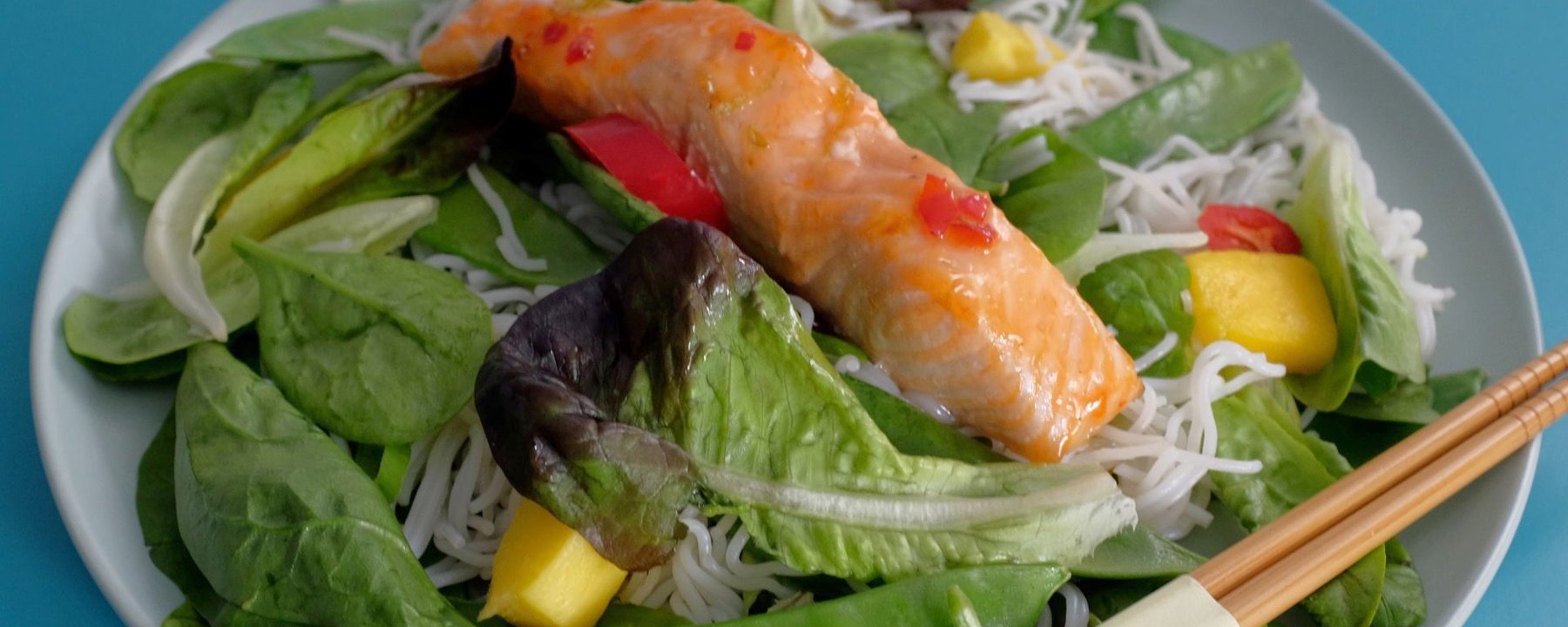 Grilled salmon fillet with rice noodles, mixed salad leaves and mango on a white plate