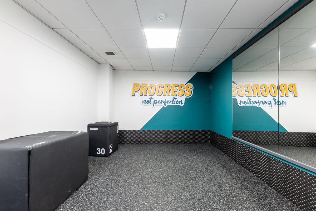 PureGym London Edgware: Grey carpeted floor, dark benches, teal accent wall with motivational text displays.
