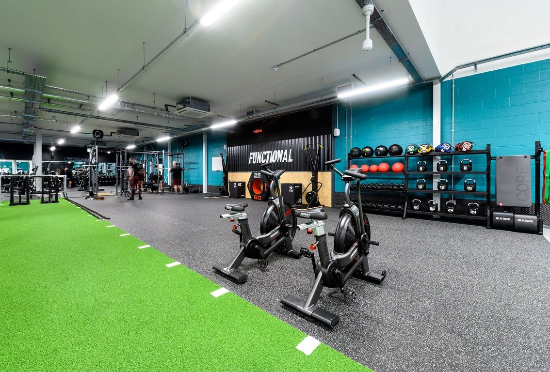 PureGym Romford: Weight benches, resistance machines, free weights, green turf area in a spacious gym setting.