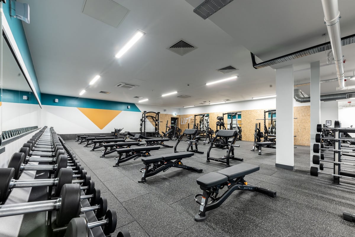 PureGym Glasgow Giffnock: Weight benches, barbells, dumbbells, plate racks on rubberized floor in bright gym space.