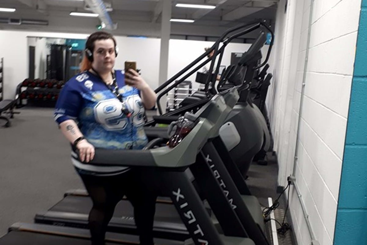 Person wearing headphones standing on a treadmill in a gym taking a mirror selfie