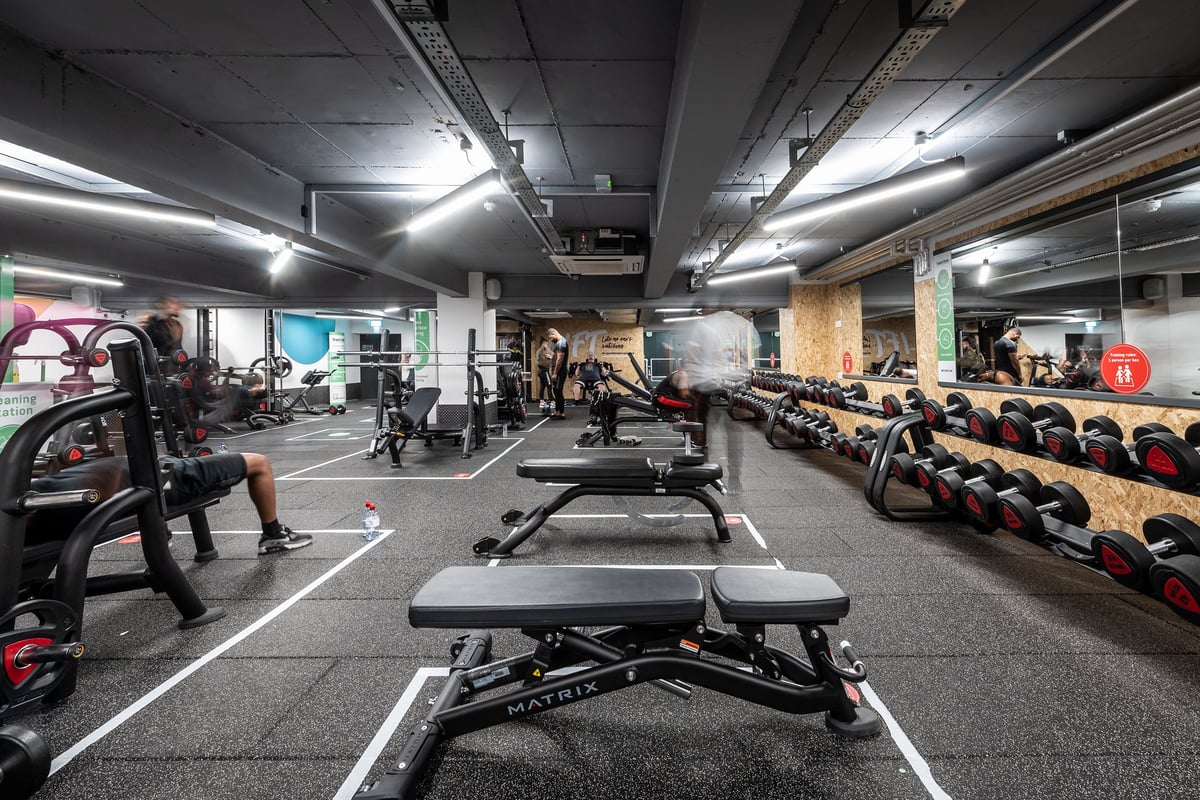 PureGym London Sydenham: Weightlifting area with benches, squat racks, dumbbells, weight plates and mirrored walls.