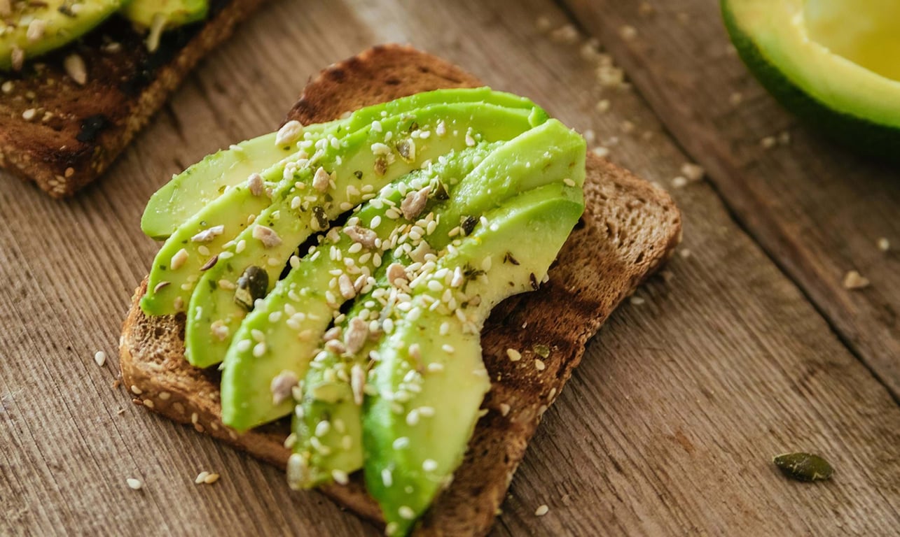 Sliced avocado on toasted whole grain bread sprinkled with seeds on wooden surface