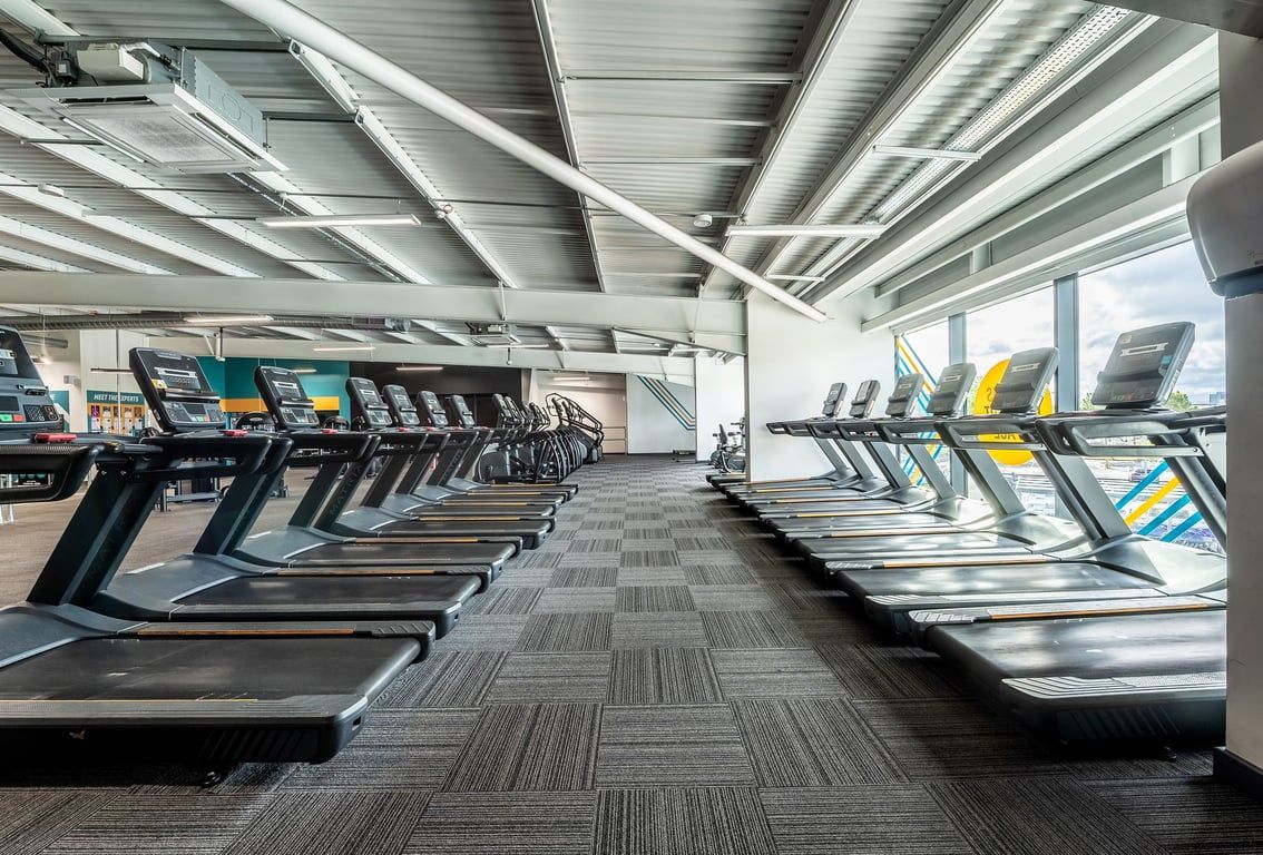 PureGym Manchester Cheetham Hill Retail Park: Rows of treadmills inside a brightly lit gym space with exposed ceiling beams.