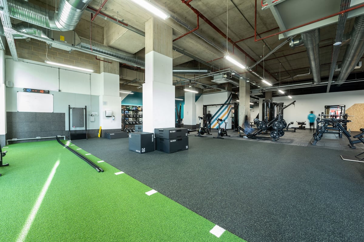 PureGym London Woolwich: Gym studio with green turf area, weight racks, exercise equipment, and rubberized flooring.