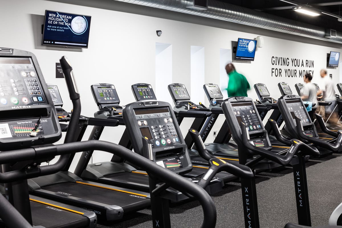 PureGym Manchester Stretford: Rows of treadmills with screens showing run stats in a fitness centre.