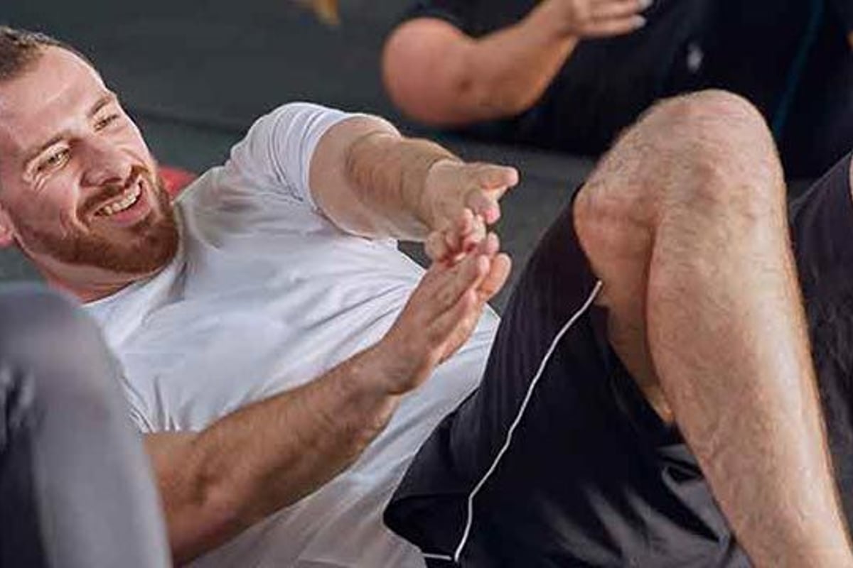 Mann führt Bauchkräftigung am Boden durch und lächelt, Trainer beobachtet