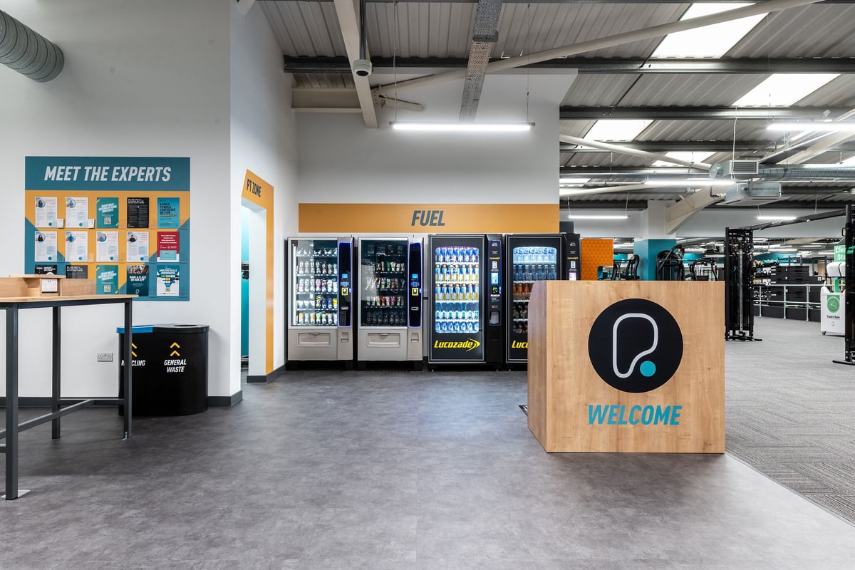 PureGym Cardiff Western Avenue: Vending machines, welcome sign, and meet the experts board in a commercial setting.