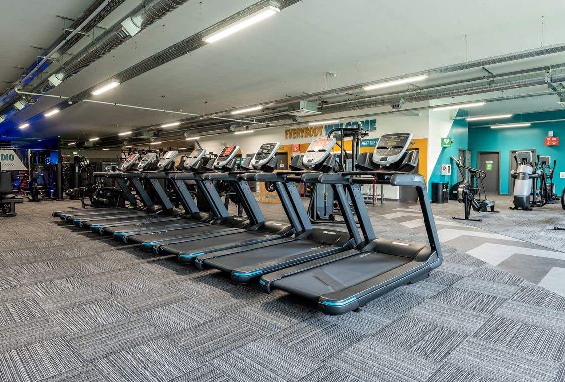 PureGym Witney: Rows of treadmills in a brightly lit gym with patterned flooring and exposed ceilings.